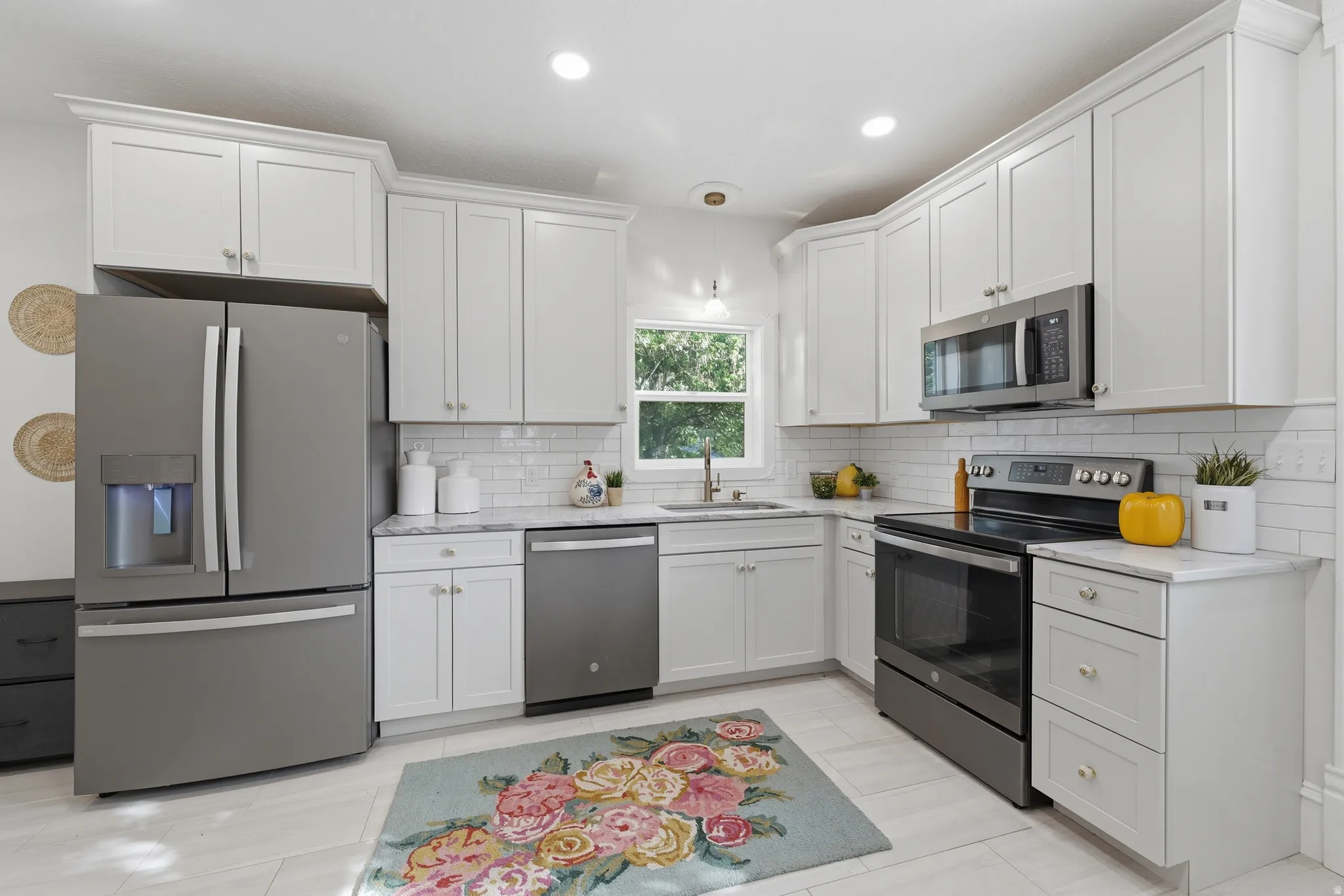 White shaker-style cabinetry with crown molding, stainless steel appliances, light-toned countertops, subway tile backsplash, and recessed lighting