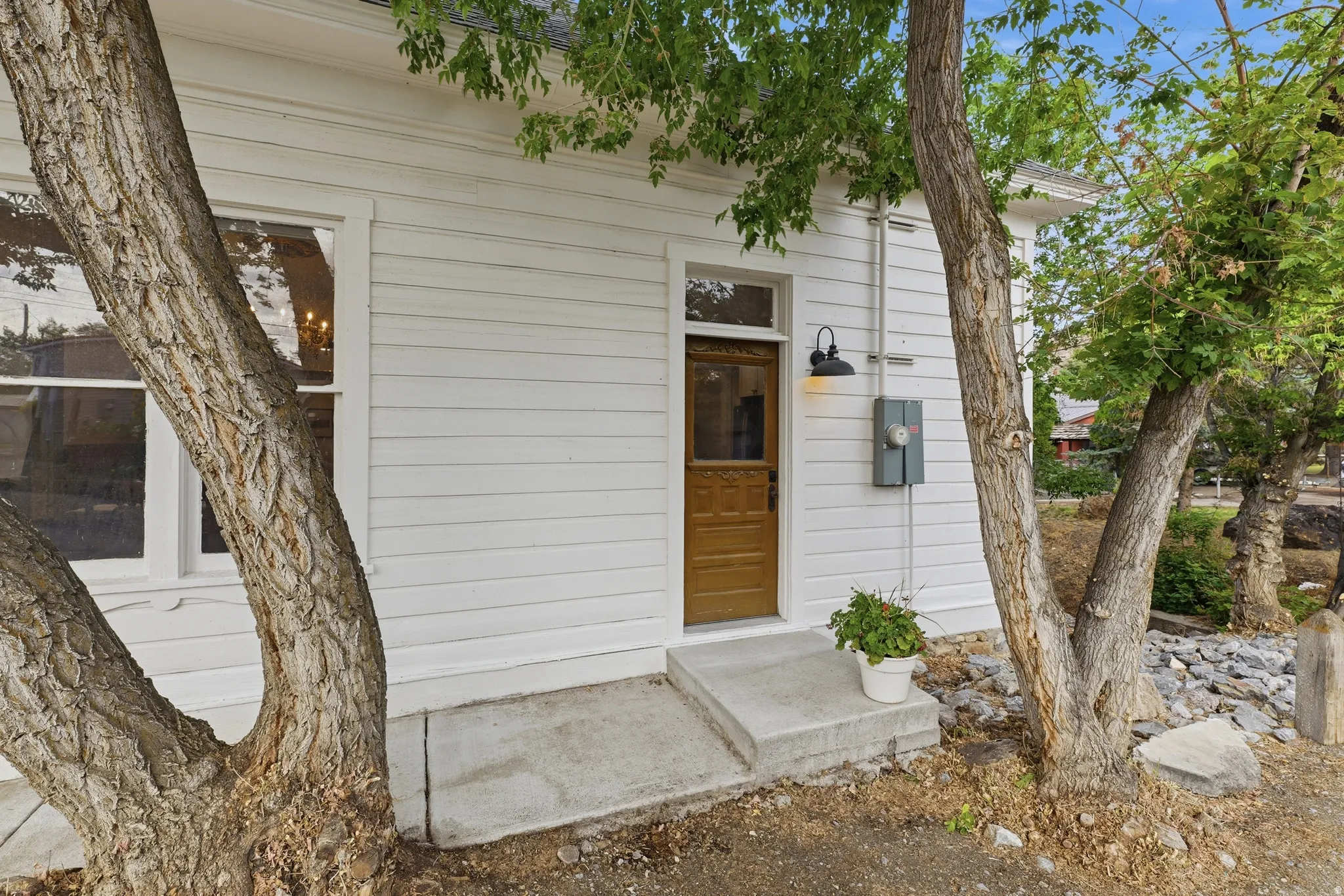 White horizontal siding with a wood-paneled door, transomed entry, and a gooseneck outdoor light fixture