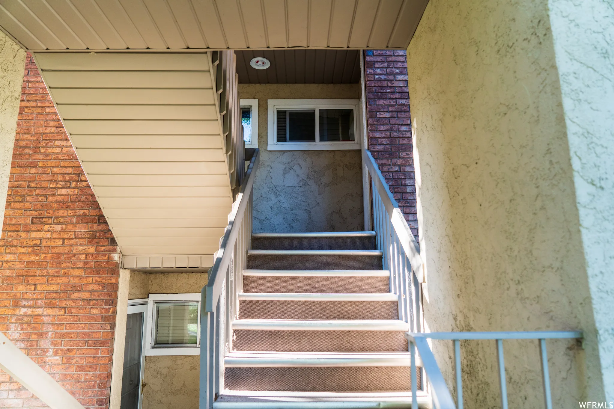 Exterior staircase featuring metal railings, textured stucco, and exposed brick accents
