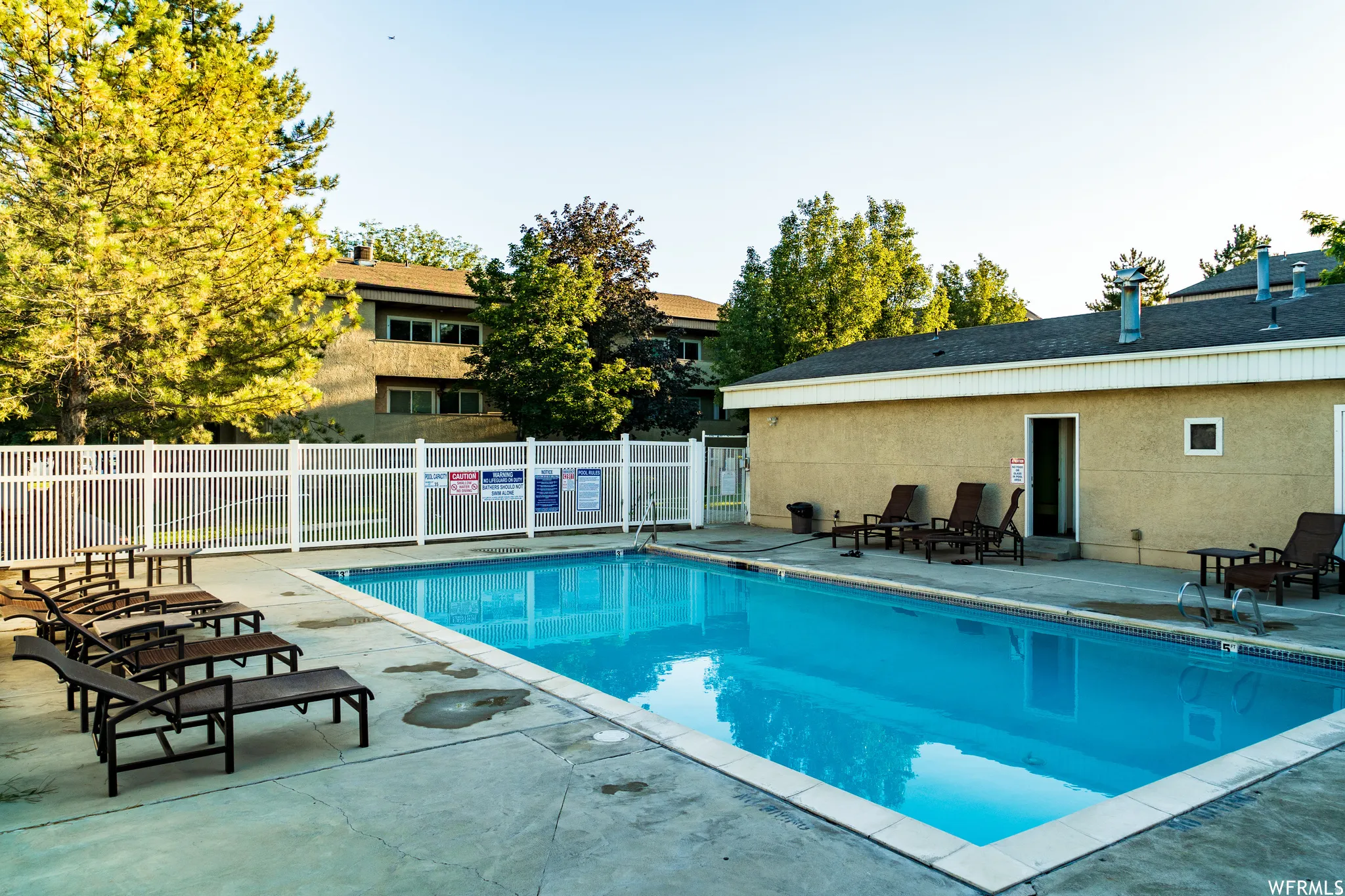 Outdoor swimming pool with a concrete surround and a white perimeter fence