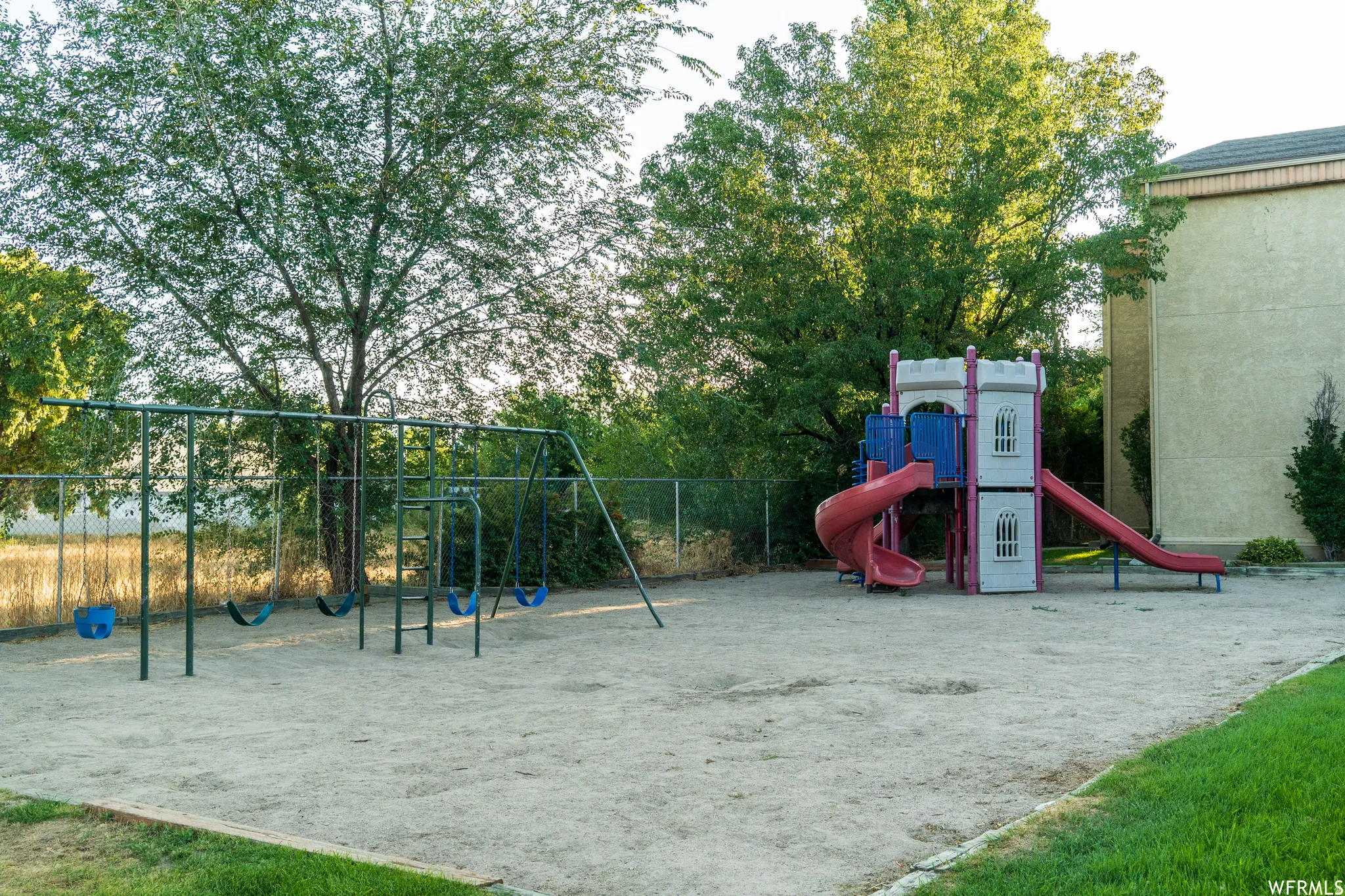 Community playground with a swing set, slide structure, and sand surface