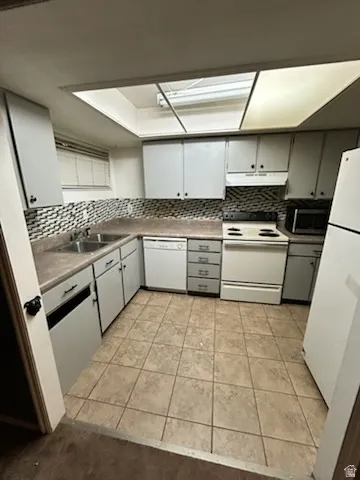 Kitchen featuring overhead lighting, tile flooring, light-toned cabinetry, an integrated dishwasher, and a microwave
