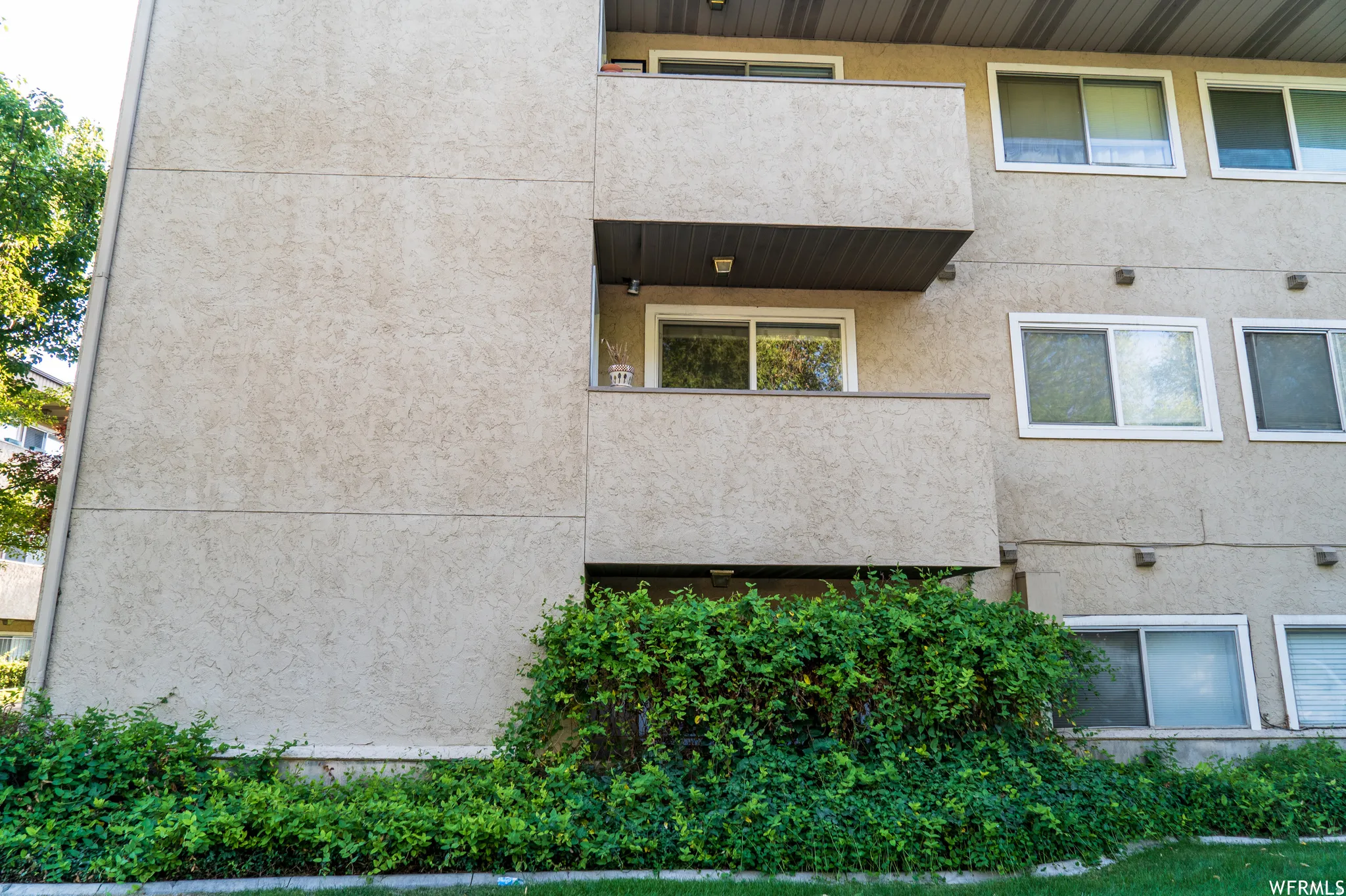 Stucco exterior with multiple balconies, white-framed windows, and ground-level plantings
