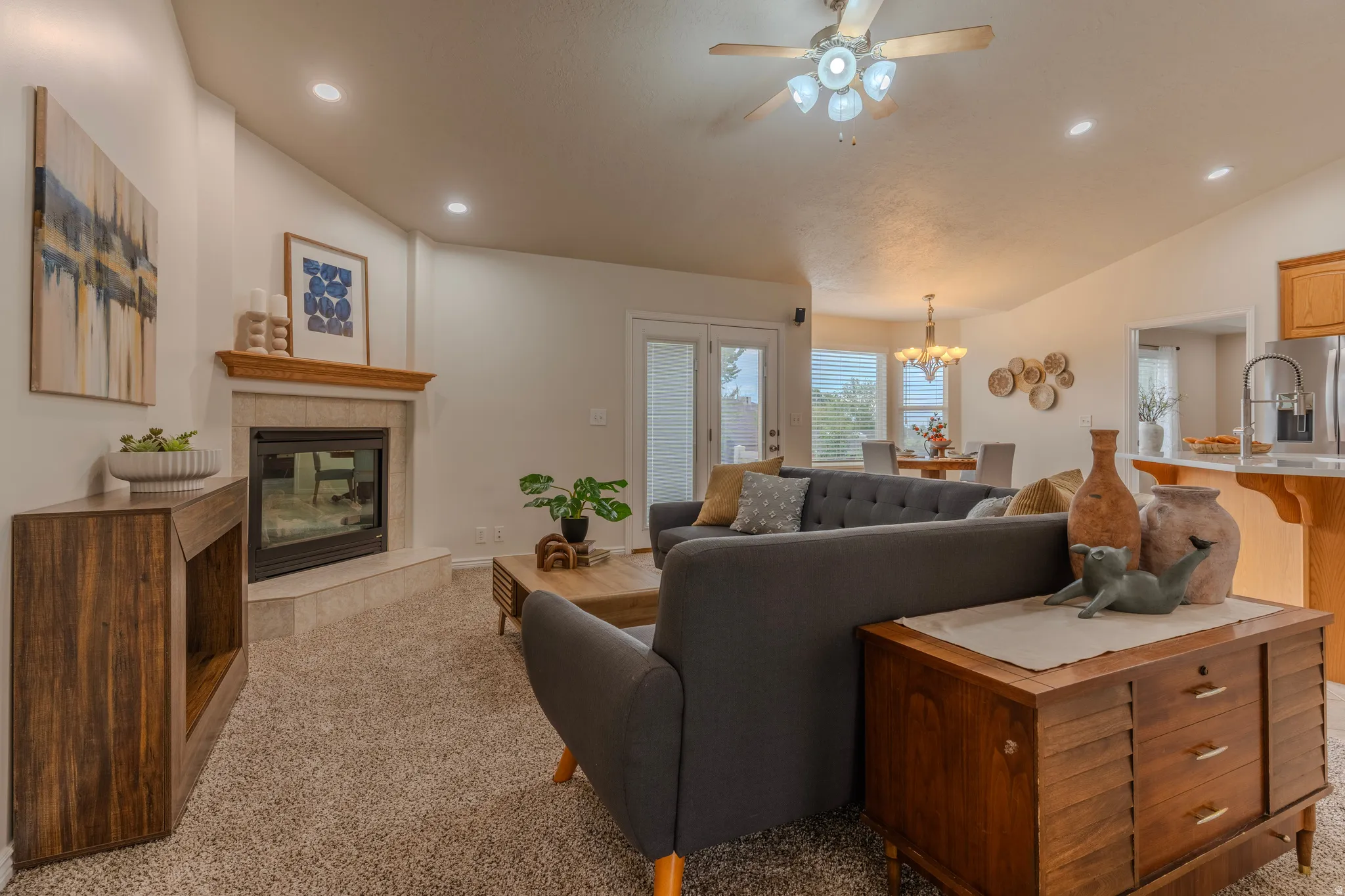 Open-concept living area featuring a gas fireplace with wood surround, ceiling fan with integrated lighting, recessed ceiling lights, and expansive windows with natural light
