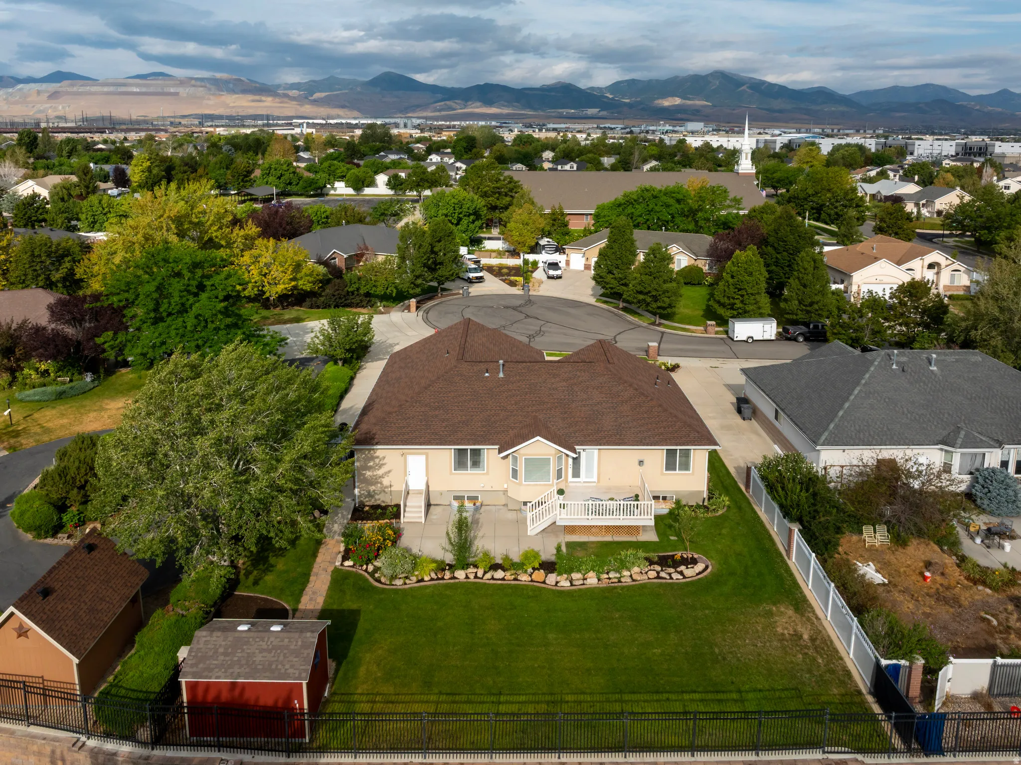Expansive green lawn, mature trees, rear deck with white railing, paved patio area, and mountain backdrop