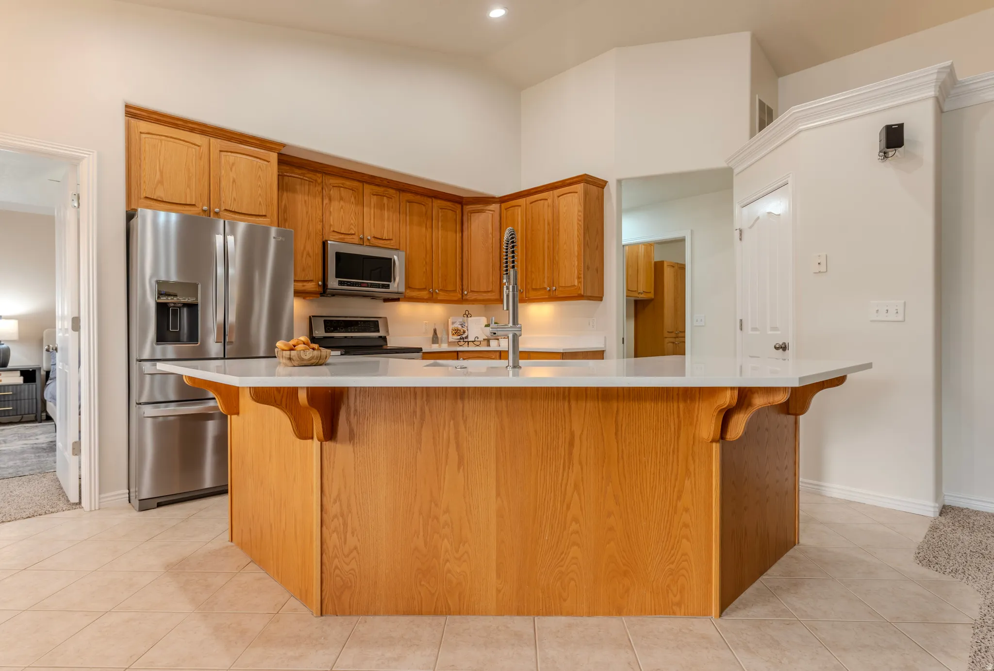 Warm wood cabinetry and island anchors this kitchen, featuring stainless steel appliances, a tile floor, and ample counter space