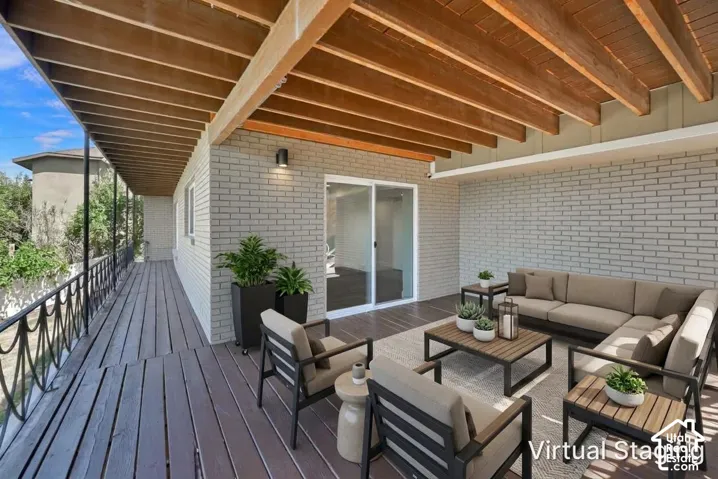 Expansive outdoor deck featuring wood-finish flooring, an exposed beam ceiling, a brick exterior wall, and sliding glass doors
