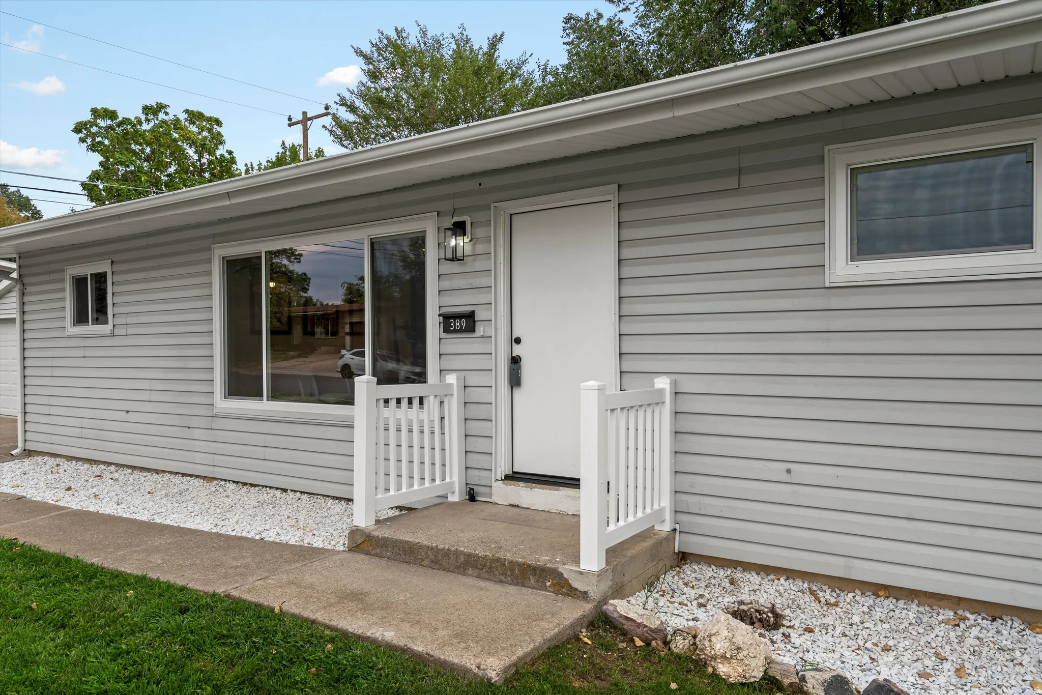 Light gray horizontal siding, concrete entry steps, white entry railing, exterior wall lantern, and white window trim