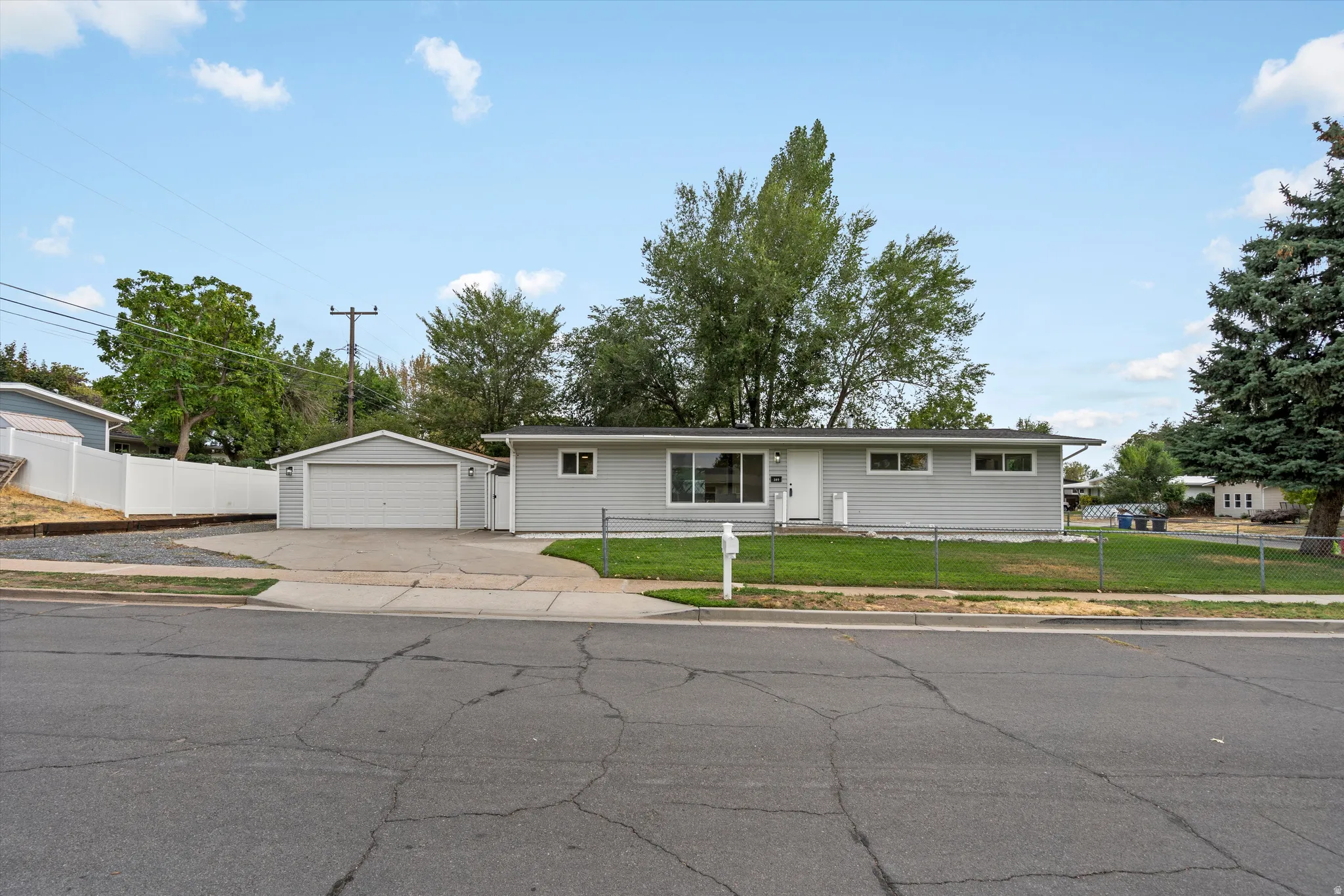 Light gray exterior with white trim, a detached two-car garage, mature front yard tree, and a concrete driveway