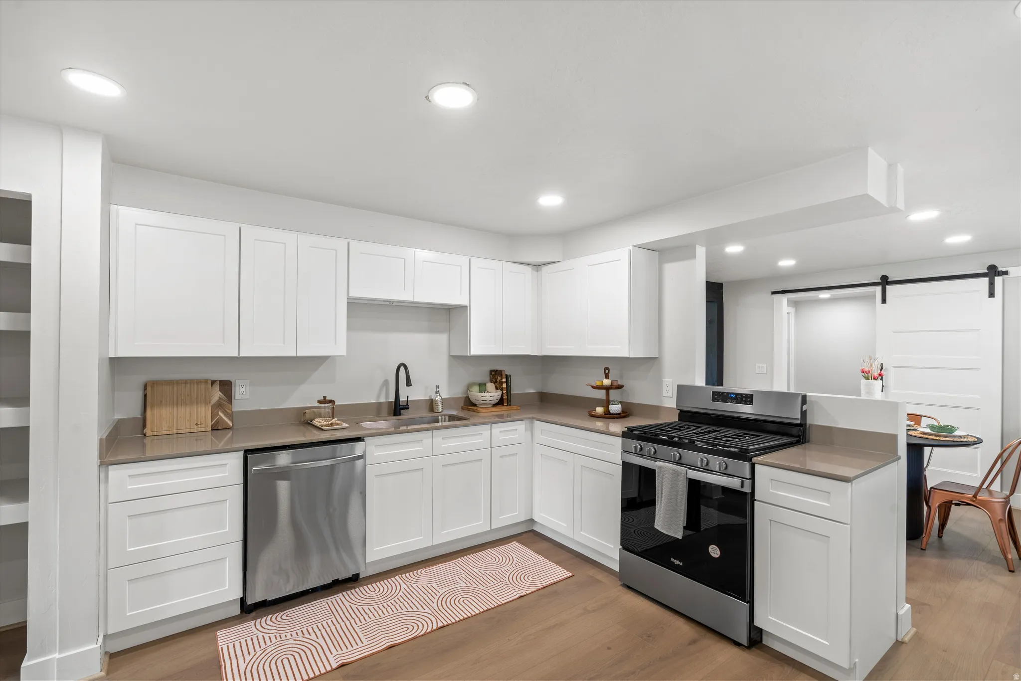 Kitchen featuring white shaker-style cabinetry, stainless steel appliances, recessed lighting, wood-finish flooring, and a sliding barn door
