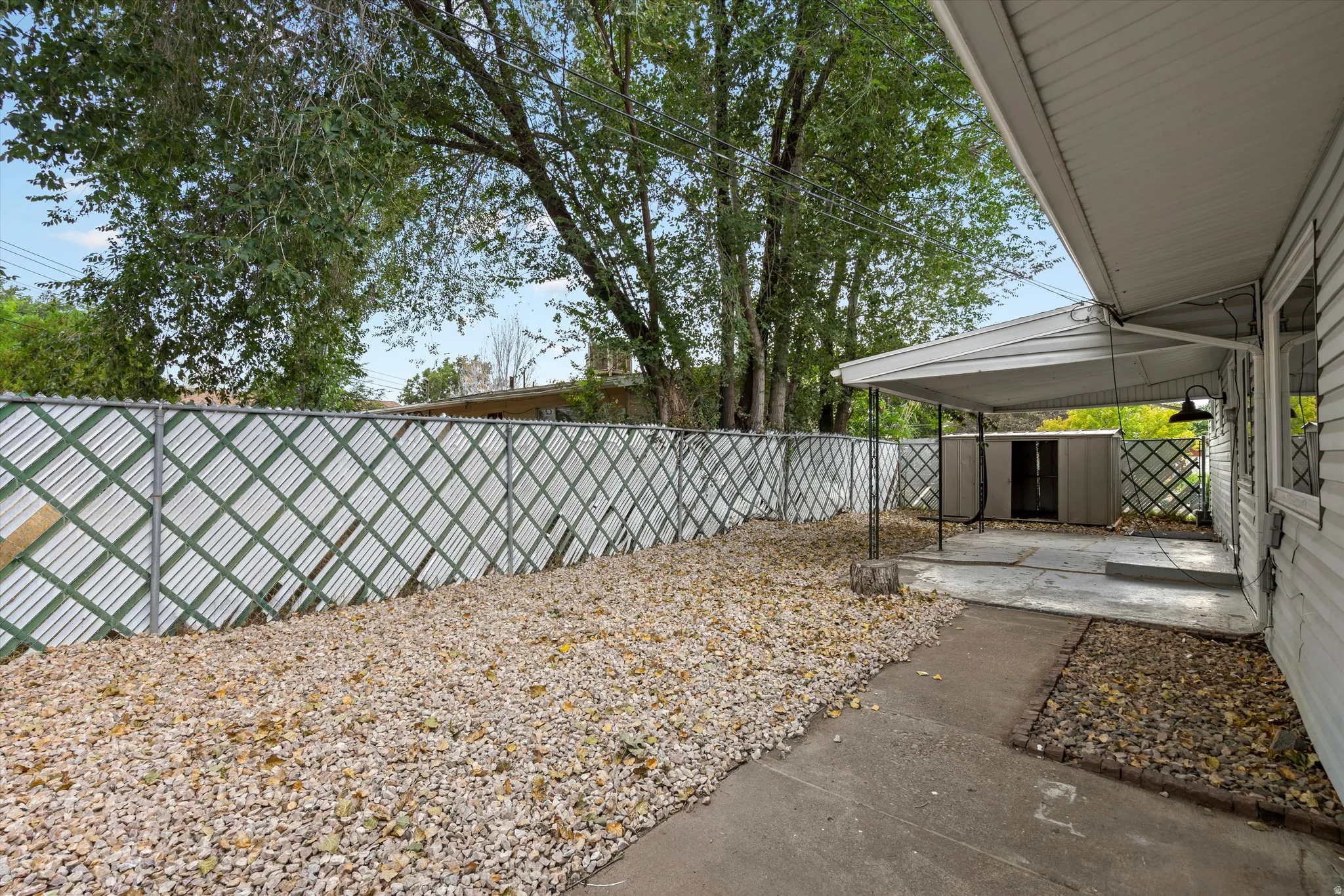 Covered patio space, gravel ground cover, metal storage shed, and mature trees