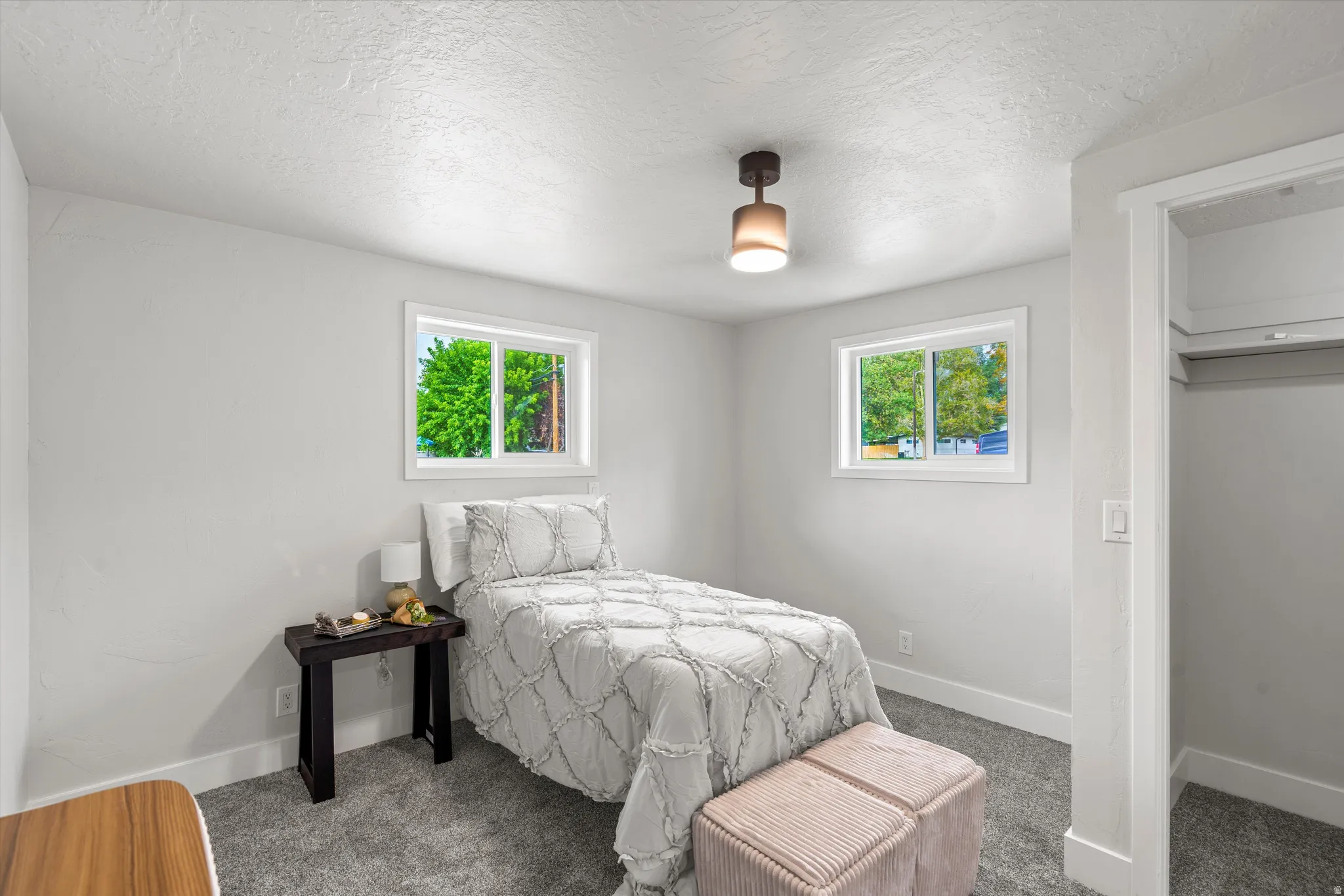 Light gray wall paint, textured ceiling, two white-framed windows, and gray carpet flooring