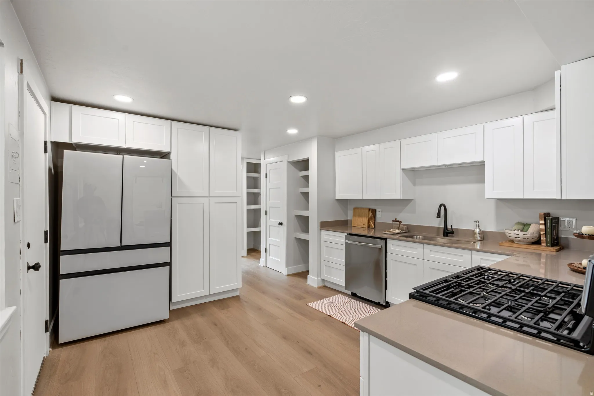 Modern kitchen featuring light wood-finish flooring, white cabinetry, integrated refrigerator, stainless steel dishwasher, and a gas range