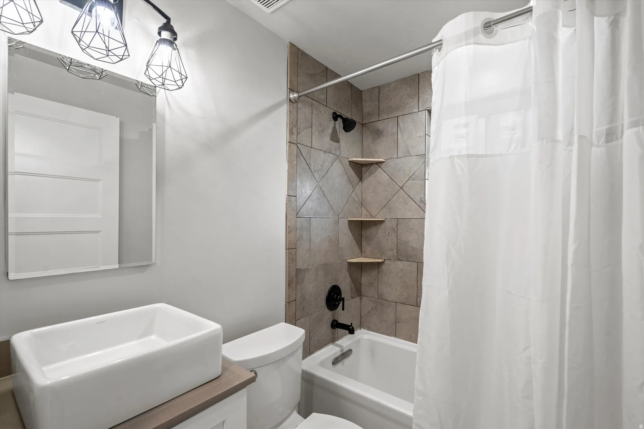 Modern vanity with a rectangular vessel sink, geometric light fixtures, and a tiled shower-tub combination with corner shelving