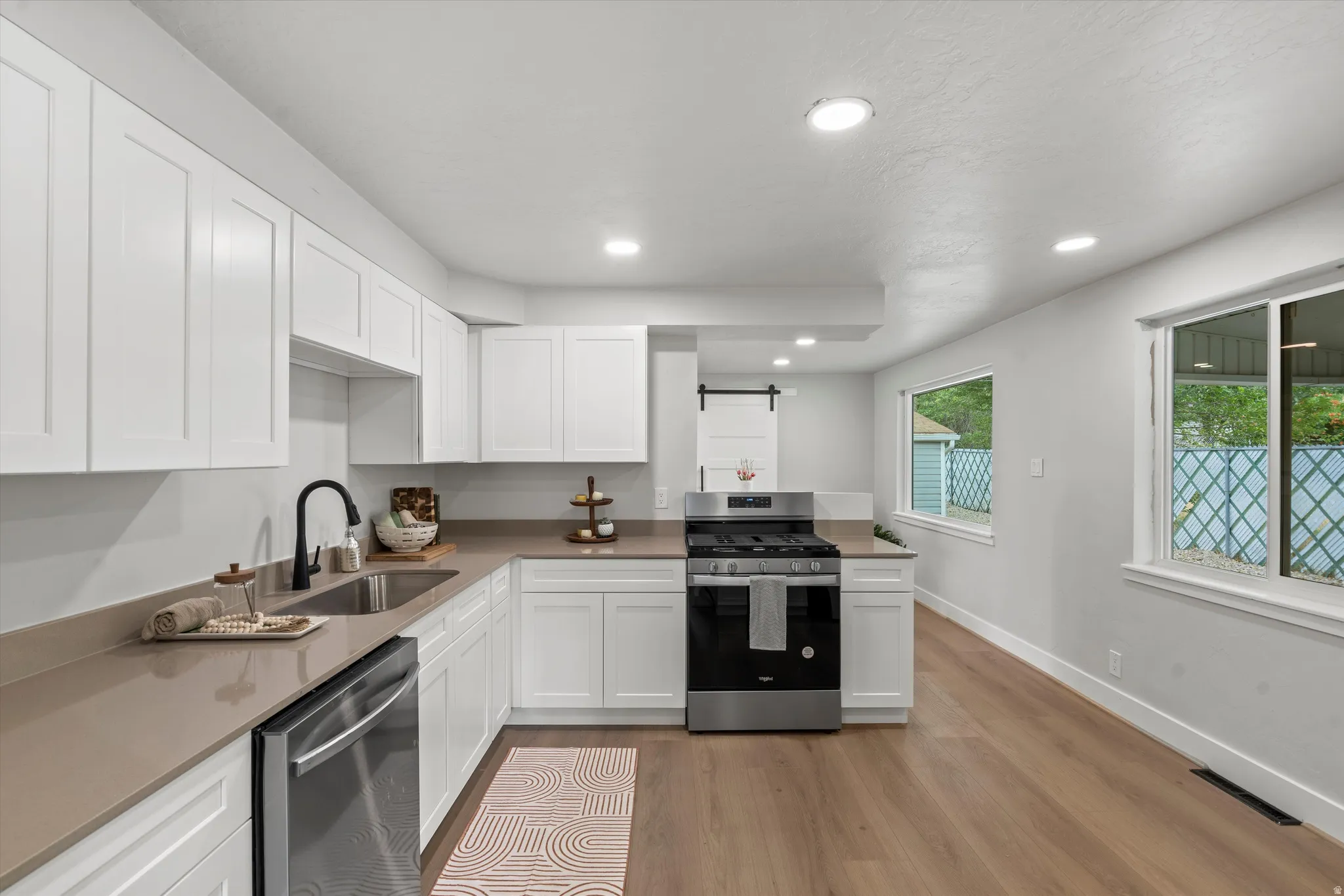 Kitchen featuring white shaker cabinetry, stainless steel appliances, neutral countertops, wood-finish flooring, and recessed lighting