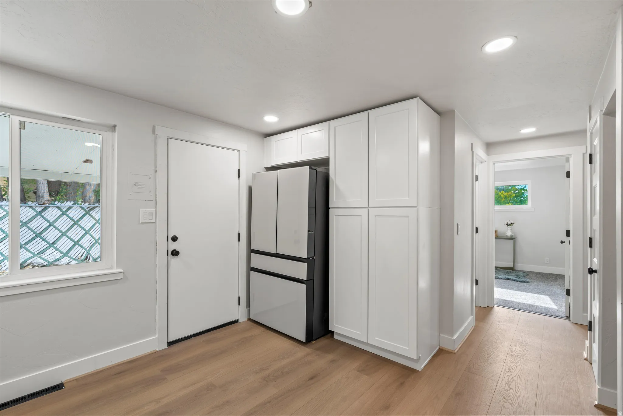 Recessed lighting, wood-finish flooring, white cabinetry, and a modern two-tone refrigerator
