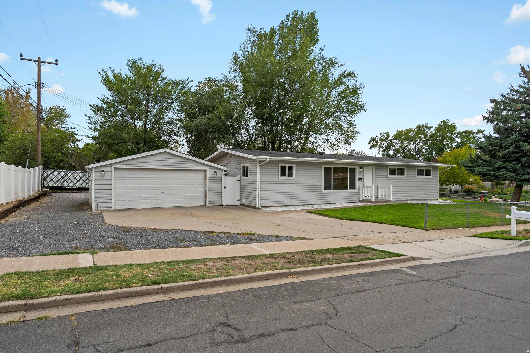 Ranch-style exterior with light gray siding, attached garage, concrete driveway, and a fenced yard