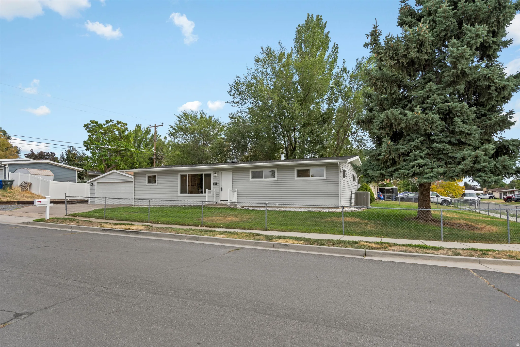Single-story residence featuring light gray siding, an attached garage, and a chain link fence