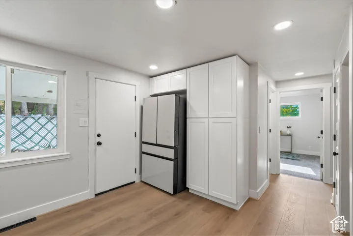 Recessed lighting, wood-finish flooring, white cabinetry, and a modern two-tone refrigerator