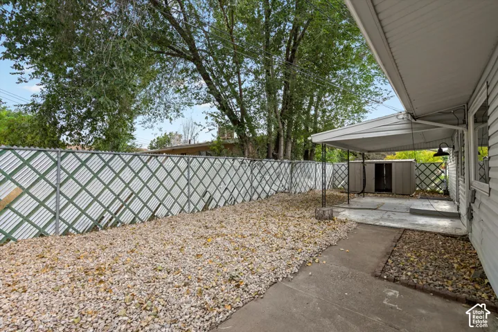 Covered patio space, gravel ground cover, metal storage shed, and mature trees