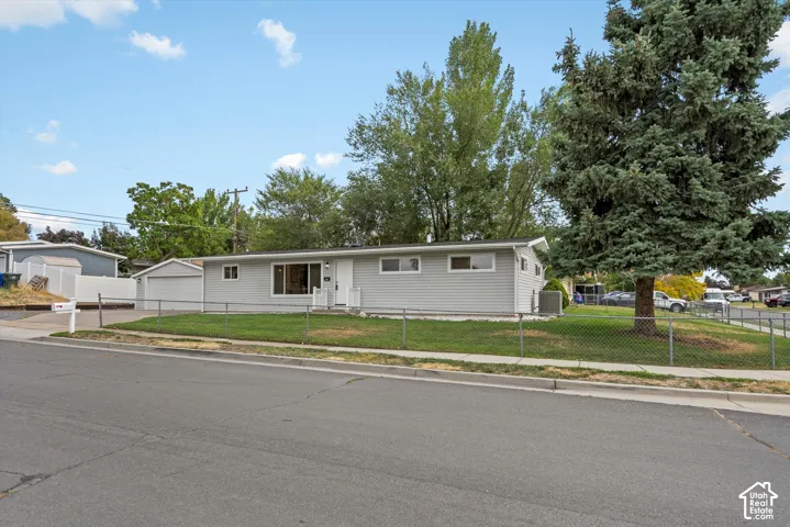 Single-story residence featuring light gray siding, an attached garage, and a chain link fence