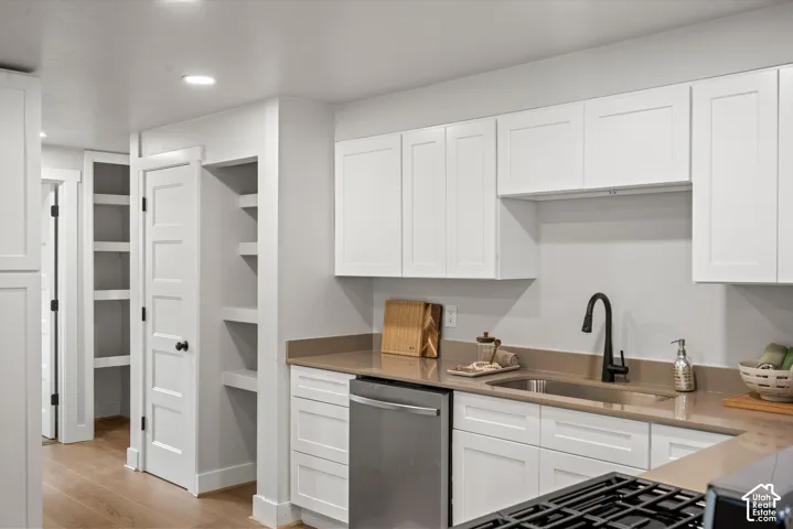 Kitchen featuring white shaker-style cabinetry, a stainless steel under-mount sink with a matte black faucet, light-toned countertops, and a built-in dishwasher