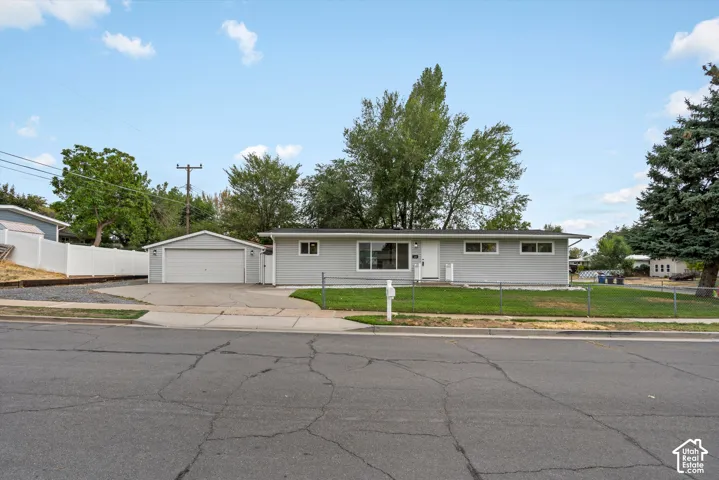 Light gray exterior with white trim, a detached two-car garage, mature front yard tree, and a concrete driveway