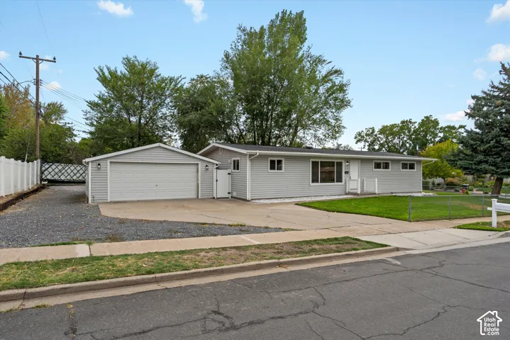 Ranch-style exterior with light gray siding, attached garage, concrete driveway, and a fenced yard