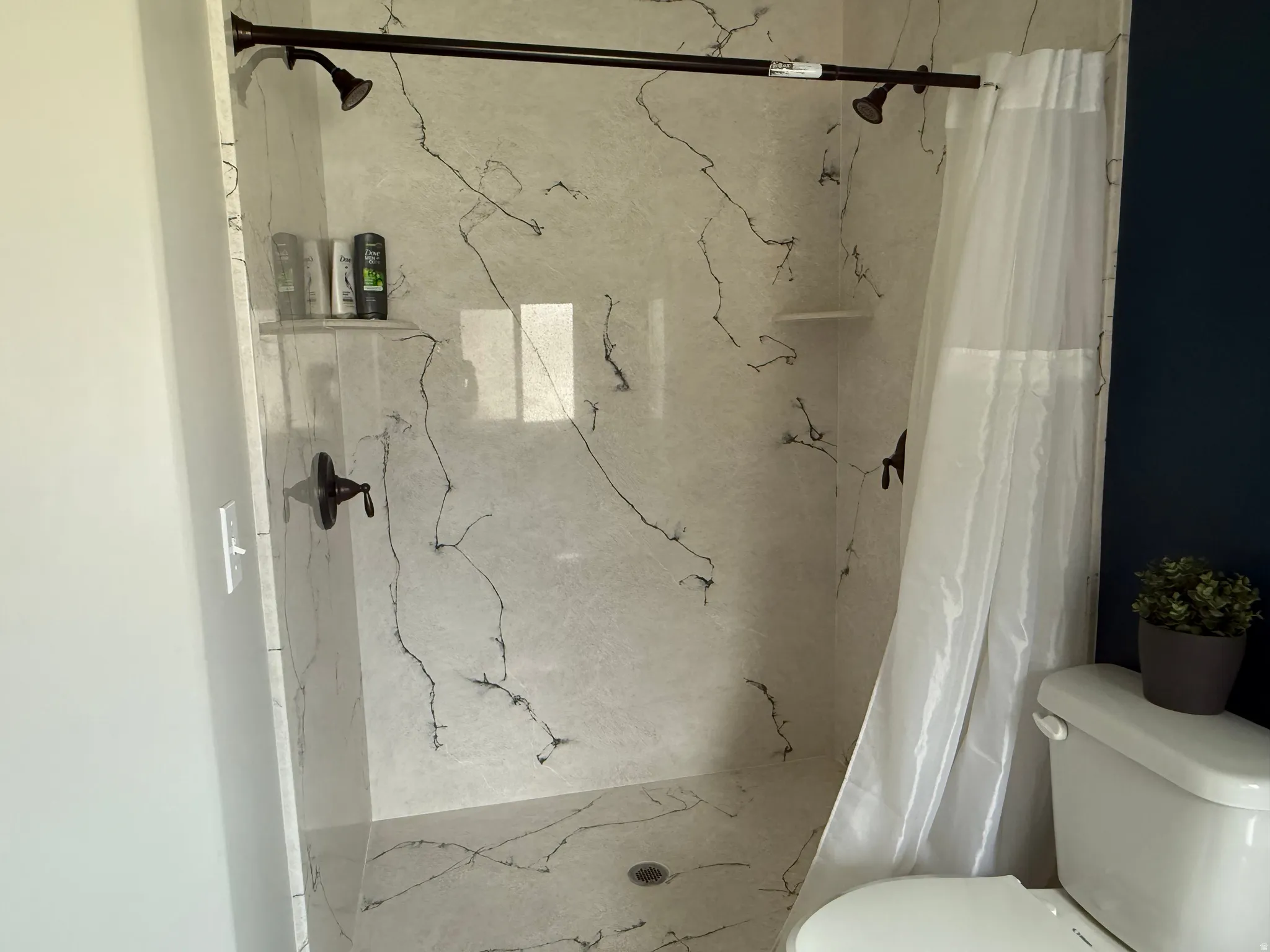 Shower stall featuring a shower head, wall-mounted faucet, and built-in shelf