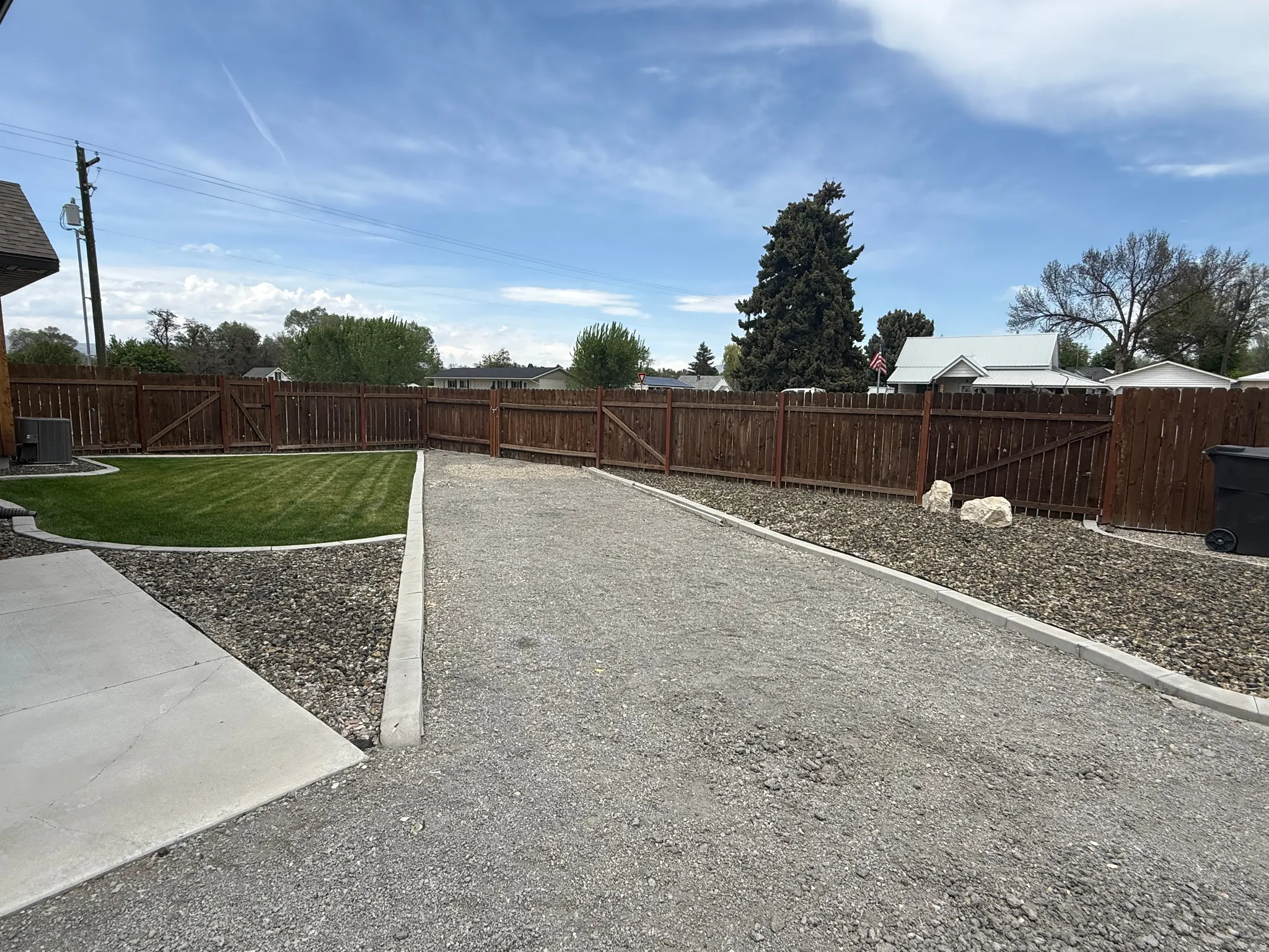 Expansive gravel area with concrete borders, manicured lawn, and wood fencing