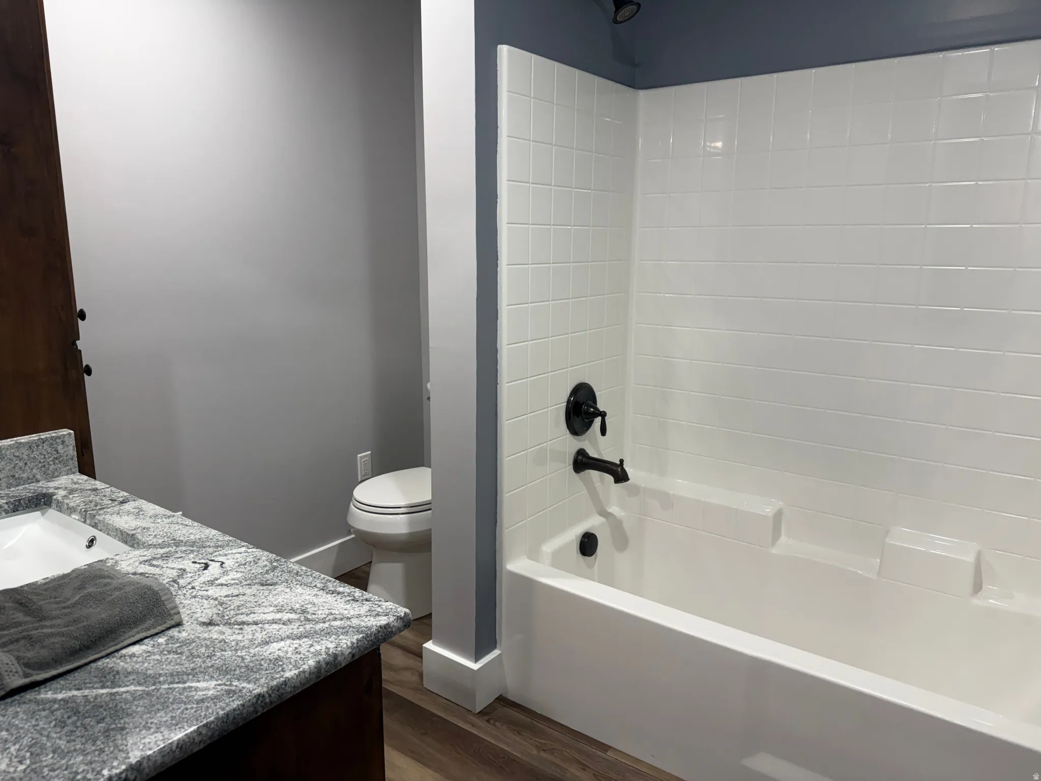 White subway tile shower surround with black fixtures, wood-finish flooring, white toilet, and a vanity with a white rectangular sink