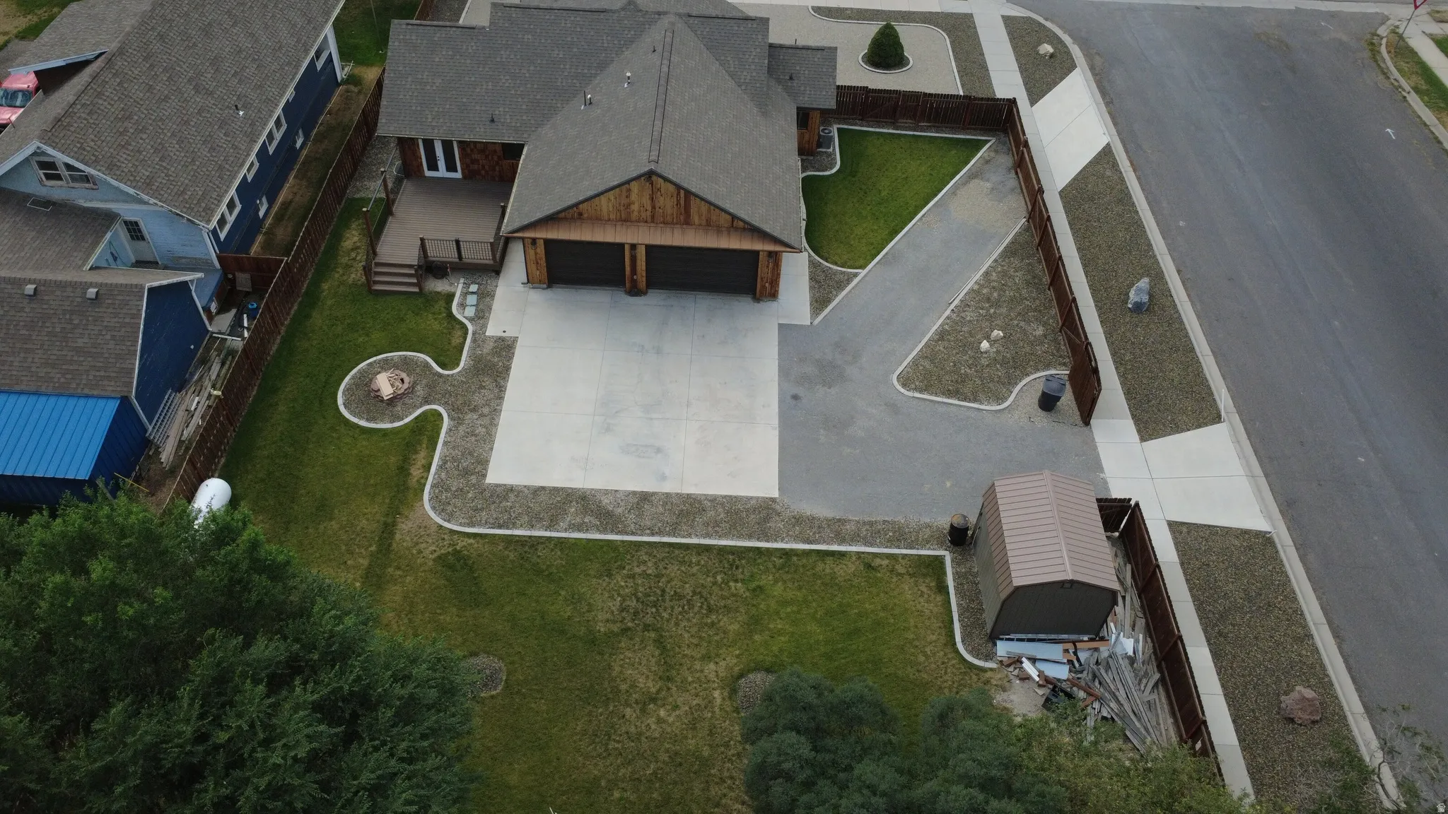 Two-car garage with wood-finish doors, expansive paved driveway, rear wood-finish deck, and a fire pit area