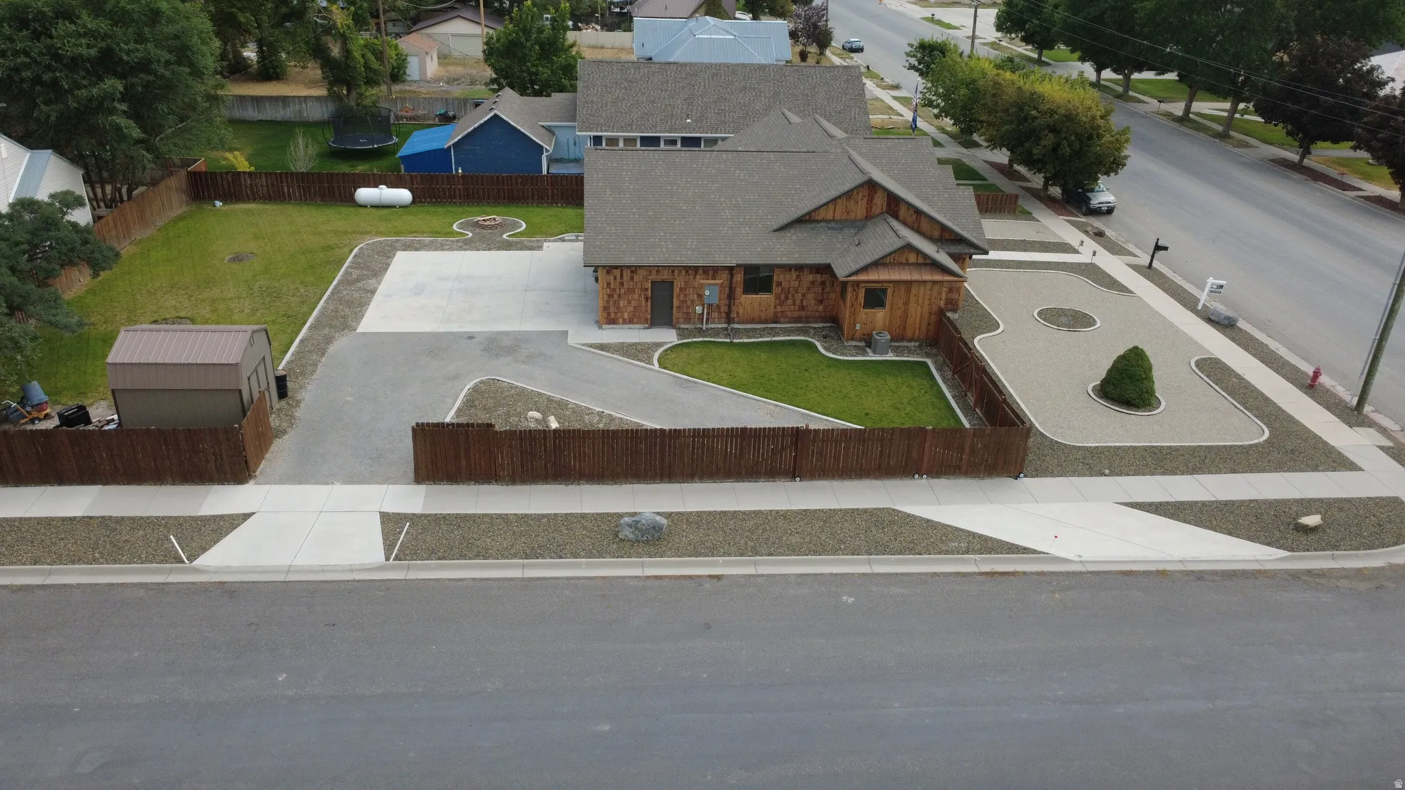 Wood-sided exterior with a shingled roof, featuring a concrete driveway, fenced yard, and a storage shed