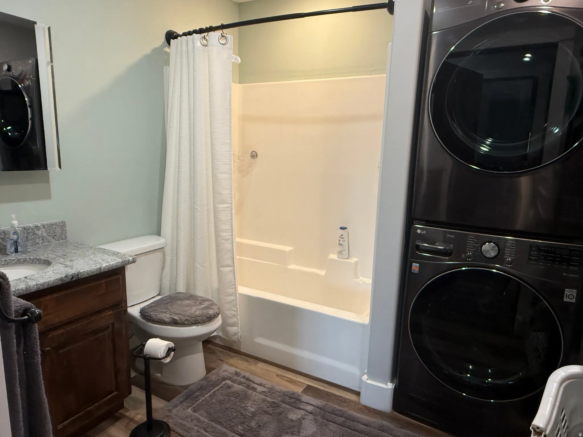 Built-in tub and shower combination, dark wood-finish vanity with stone countertop, front-loading washer and dryer, and wood-finish flooring