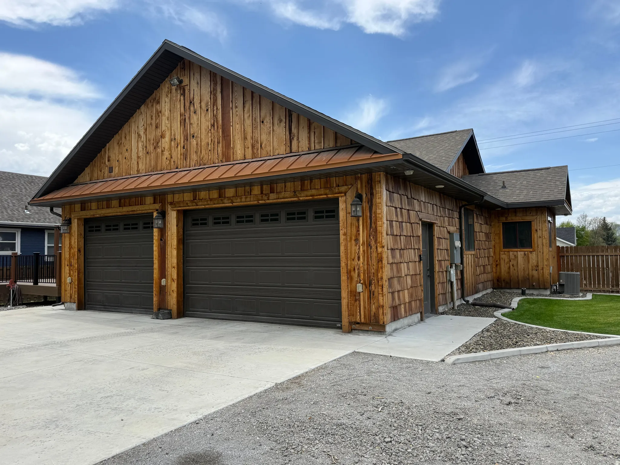 Wood-paneled exterior with shake siding, two-car garage, concrete driveway, and gravel landscaping