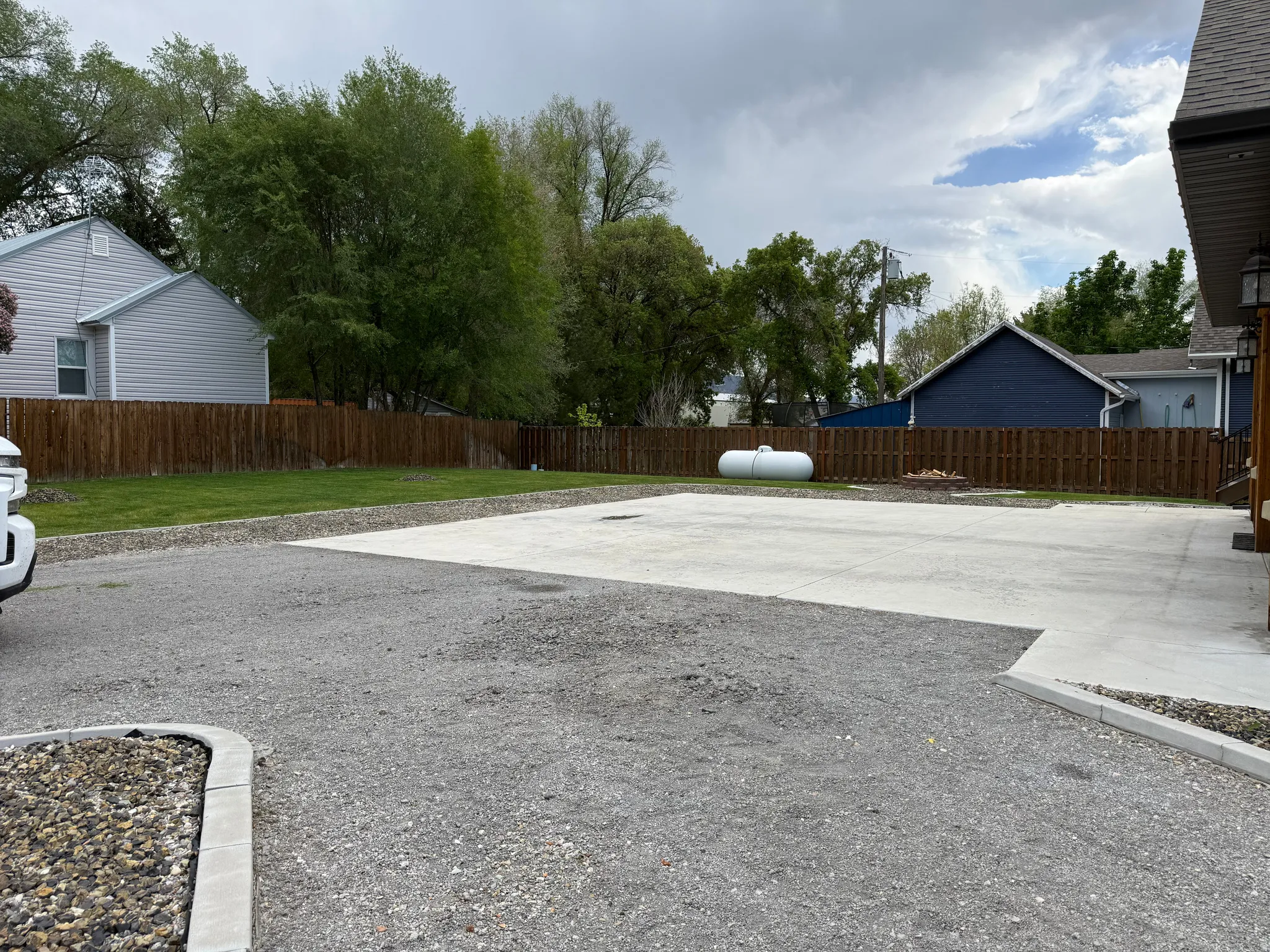 Expansive gravel driveway with a concrete parking pad, featuring a wood privacy fence and a dedicated fire pit area