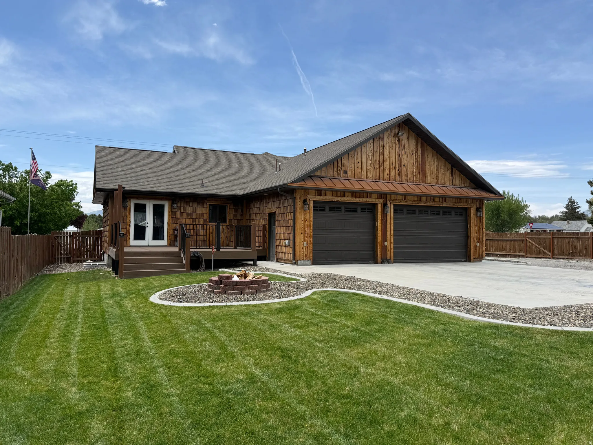 Wood-sided exterior with a shingle roof, double garage with dark doors, concrete driveway, and a backyard deck with stairs