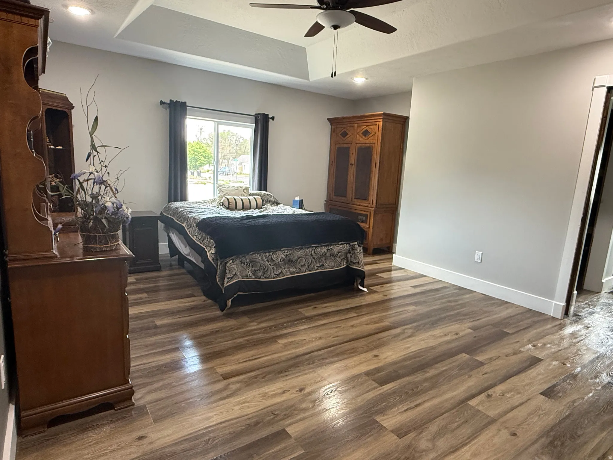 Wood-finish flooring, tray ceiling, recessed lighting, ceiling fan, and sliding glass door
