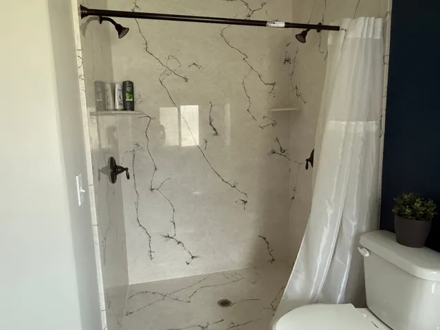 Shower stall featuring a shower head, wall-mounted faucet, and built-in shelf