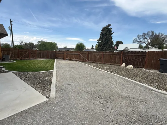 Expansive gravel area with concrete borders, manicured lawn, and wood fencing