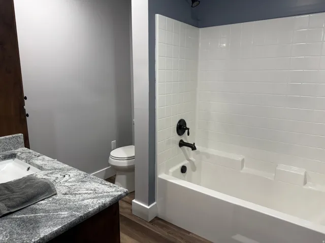 White subway tile shower surround with black fixtures, wood-finish flooring, white toilet, and a vanity with a white rectangular sink
