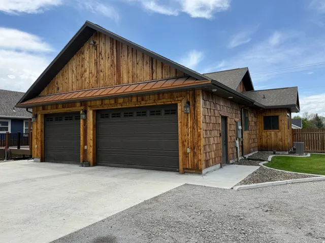 Wood-paneled exterior with shake siding, two-car garage, concrete driveway, and gravel landscaping
