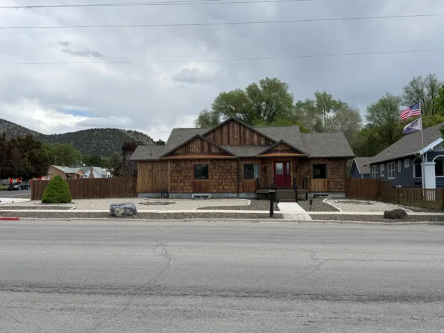 Wood-clad exterior with a red entry door, established landscaping, and a mountain backdrop