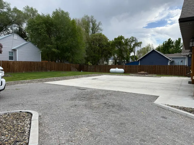 Expansive gravel driveway with a concrete parking pad, featuring a wood privacy fence and a dedicated fire pit area