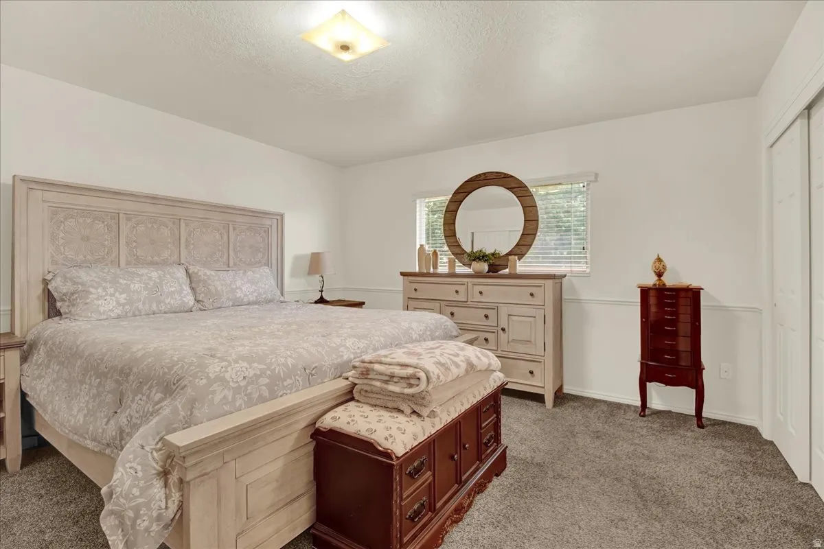Spacious primary bedroom featuring a decorative headboard with paneled detailing, neutral upholstered bedding, wood-finish dresser with multiple drawers, and abundant natural light from a large window