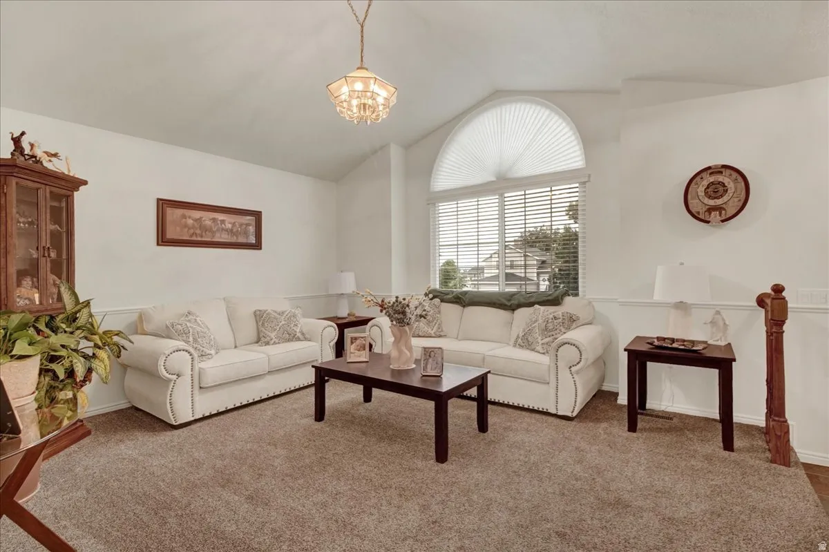 Vaulted ceiling with an ornate chandelier, large arched window, half-wall wainscoting, and carpeted flooring