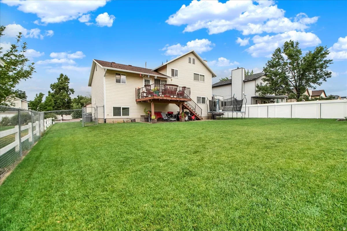 Expansive lawn with a chain-link fence, white vinyl privacy fence, and rear deck with stairs