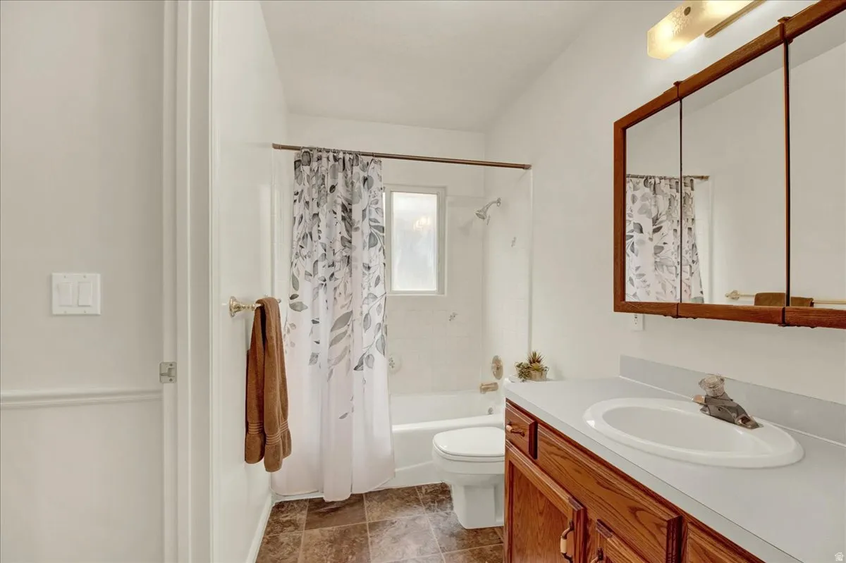 Full bathroom featuring a wood-finish vanity with dual white oval sinks, ceramic tile flooring, white subway tile walls, a toilet, and a framed mirror with wood trim
