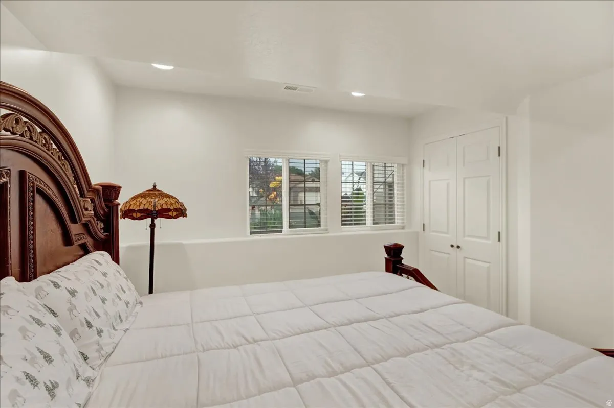 Spacious primary bedroom featuring elegant wood-finish headboard with carved detailing, recessed ceiling lighting, plantation shutters, and dual closet doors