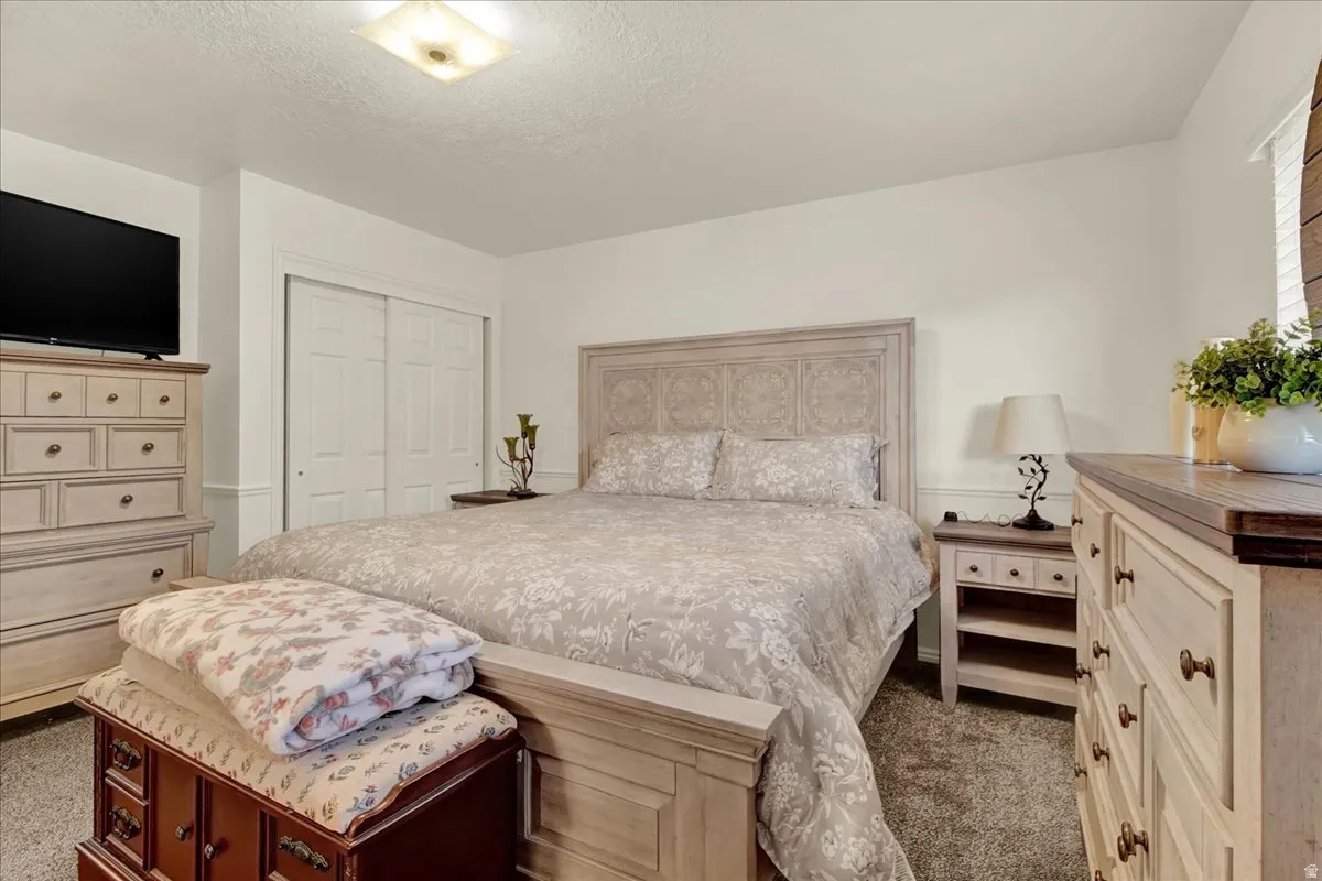 Spacious primary bedroom featuring a wood-finish bed frame with upholstered headboard, dual nightstands with storage, carpet flooring, and abundant natural light from windows